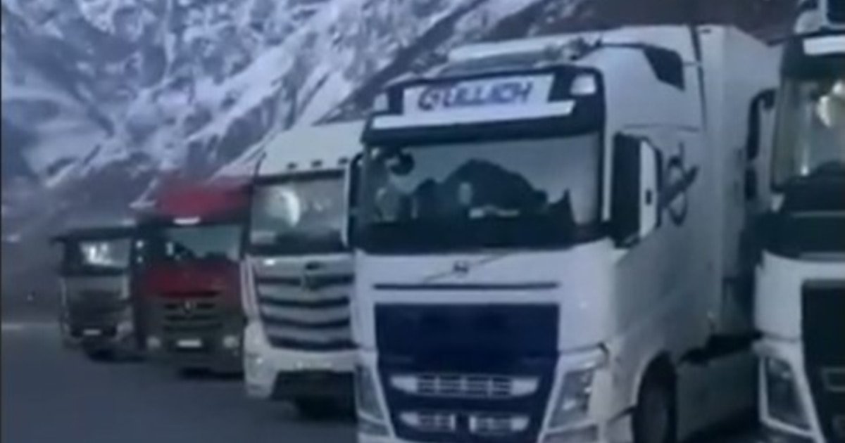 Row of trucks lined up on mountain road with snowy peaks in background