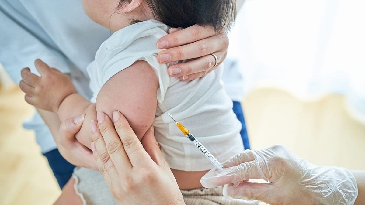 Mother holding infant receiving vaccination from healthcare worker with gloved hands