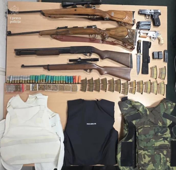 Официальное полицейское фото с изъятыми винтовками, пистолетами, боеприпасами и тремя бронежилетами, разложенными на столе
