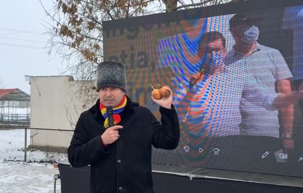 Мужчина выступает на митинге фермеров с LED-экраном — общий план, показывающий контекст протестного митинга с луком как символом