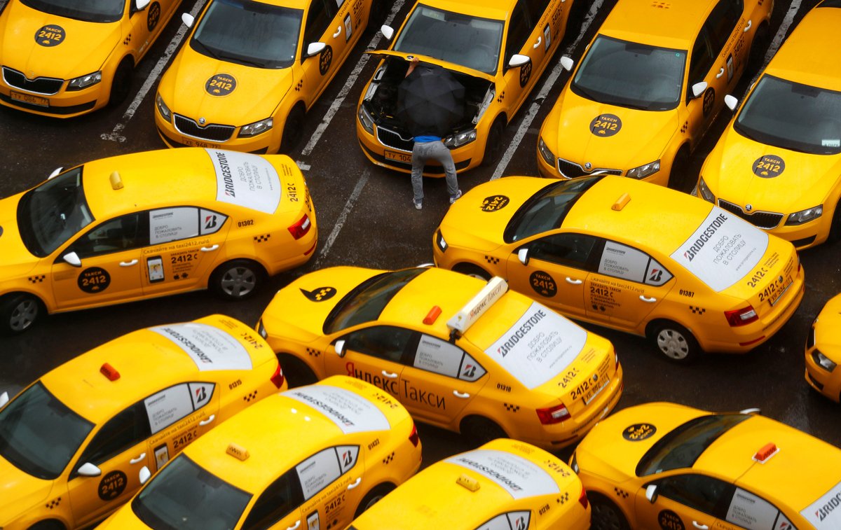 Вид сверху на множество желтых такси Яндекс, припаркованных на стоянке, показывает масштаб таксопарка