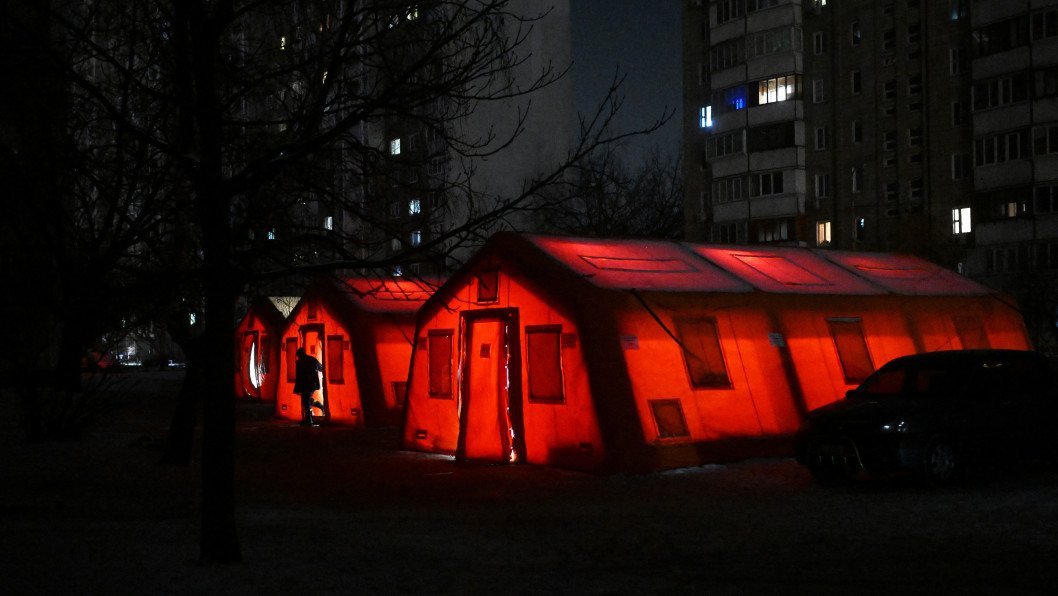 Палатка обогрева светится ночью рядом с погружёнными в темноту жилыми домами во время блэкаута