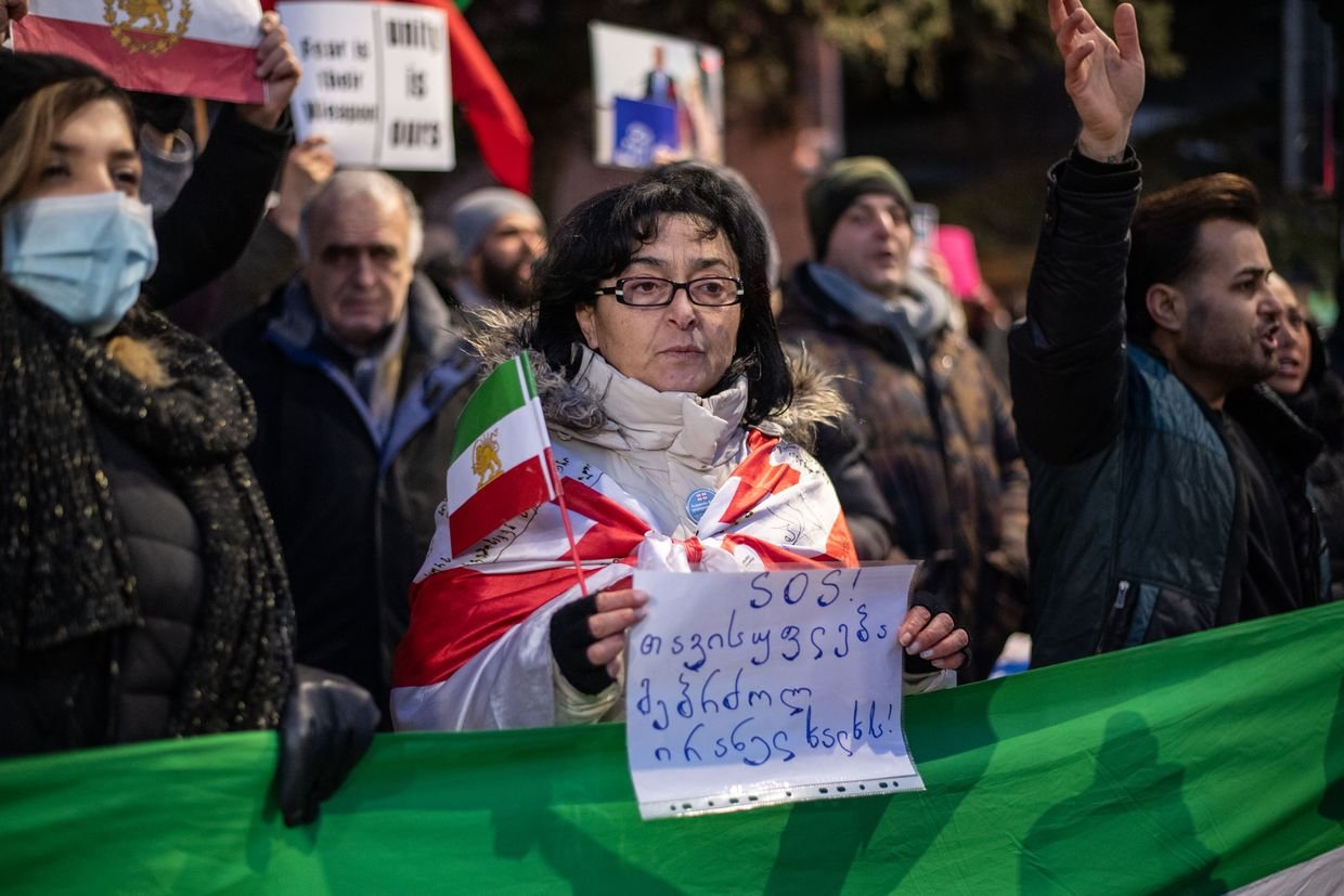 Protest in Tbilisi supporting Iranian people, woman wrapped in Georgian and Iranian flags holding SOS sign