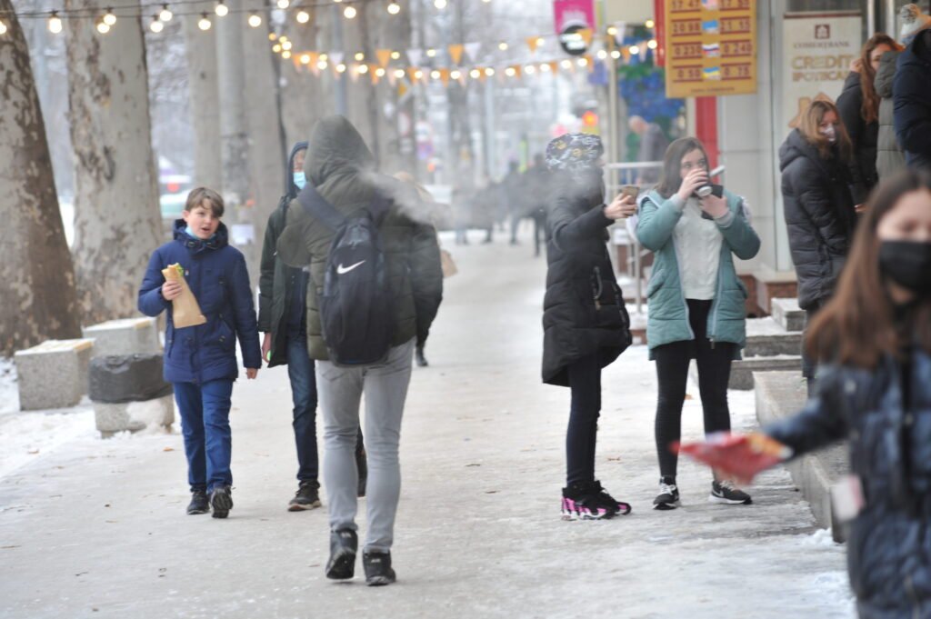 Молодые люди идут по заснеженной городской улице Молдовы зимой — контекст повседневной жизни граждан, затронутых проблемами цен на продукты