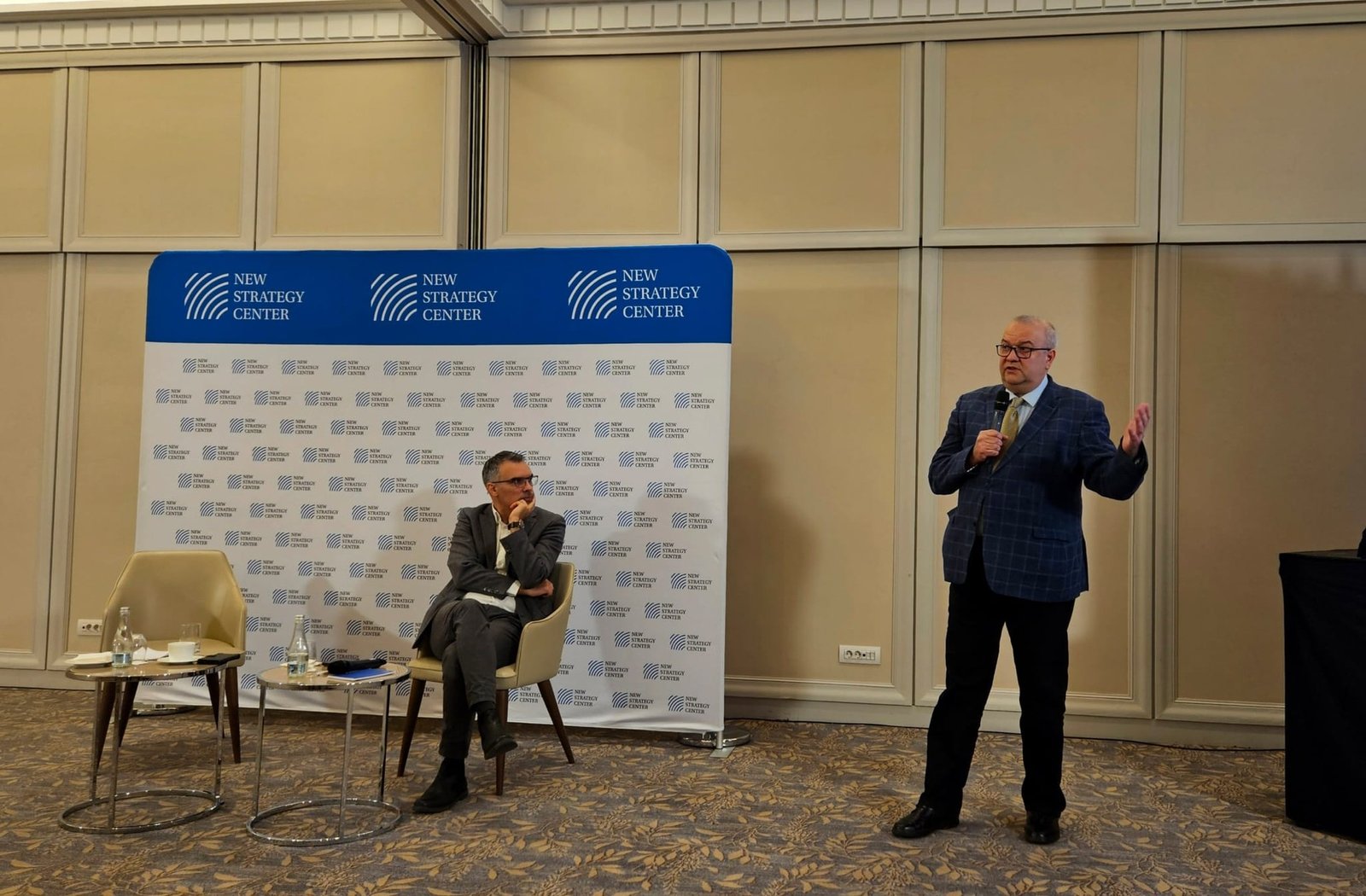 Спикер выступает на конференции New Strategy Center на фоне баннера NSC