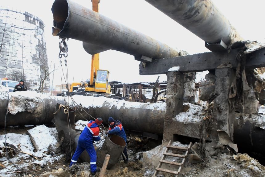 Workers repairing damaged energy infrastructure pipes with crane in winter conditions