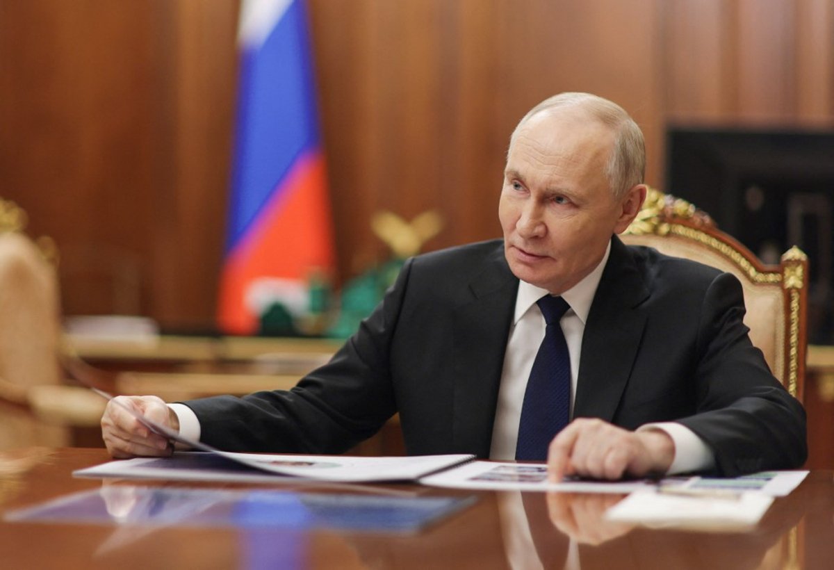 Vladimir Putin sitting at desk in the Kremlin with Russian flag behind