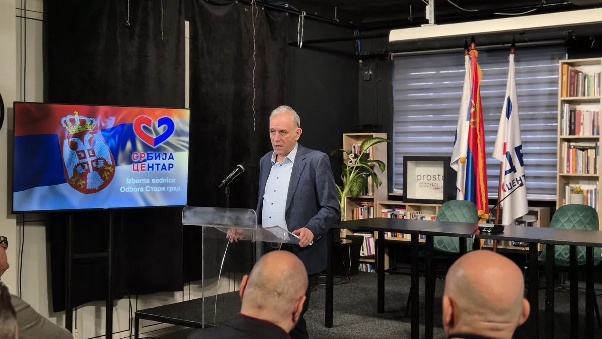 Выступающий на мероприятии партии «Сербия Центр» за трибуной, на экране позади — логотип партии
