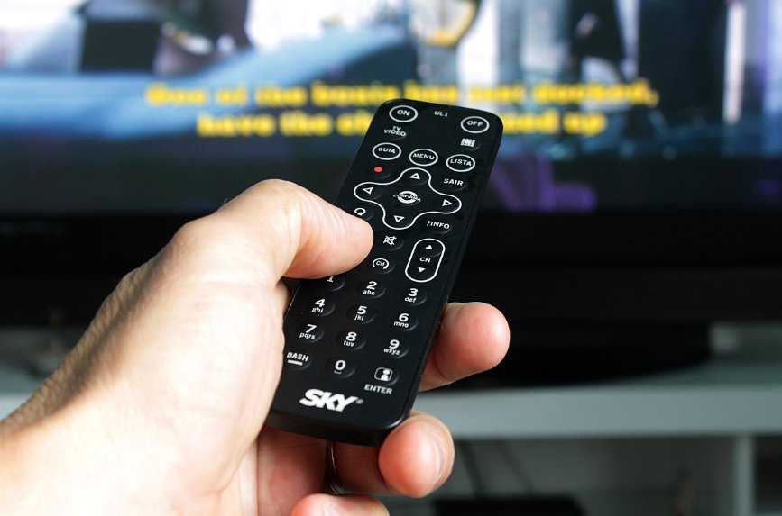 Hand holding TV remote control pointing at a television screen — symbolic image for broadcasting and media