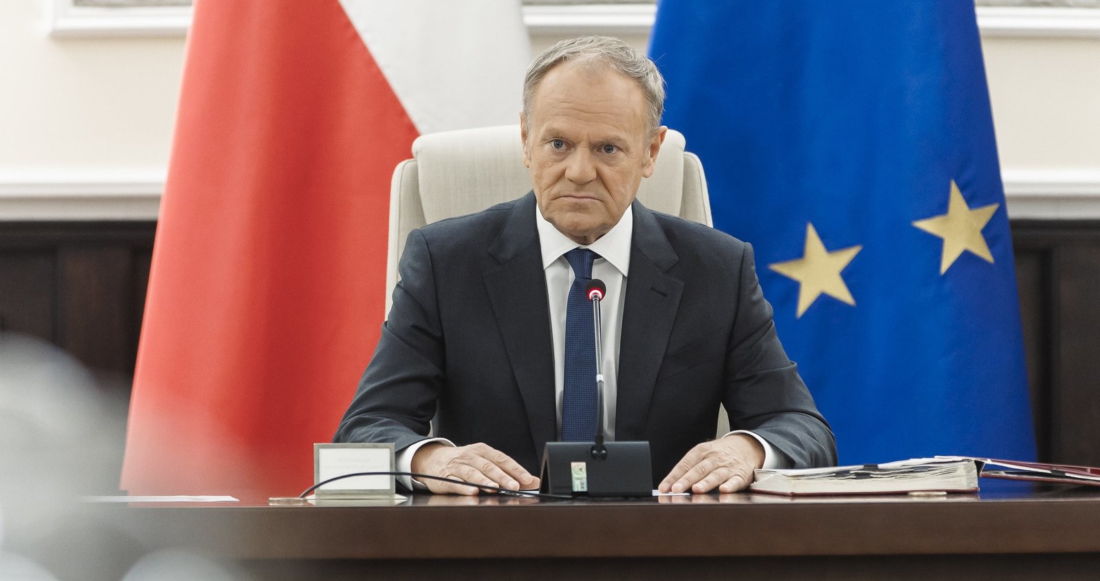 Donald Tusk sitting at desk with Polish and EU flags behind him