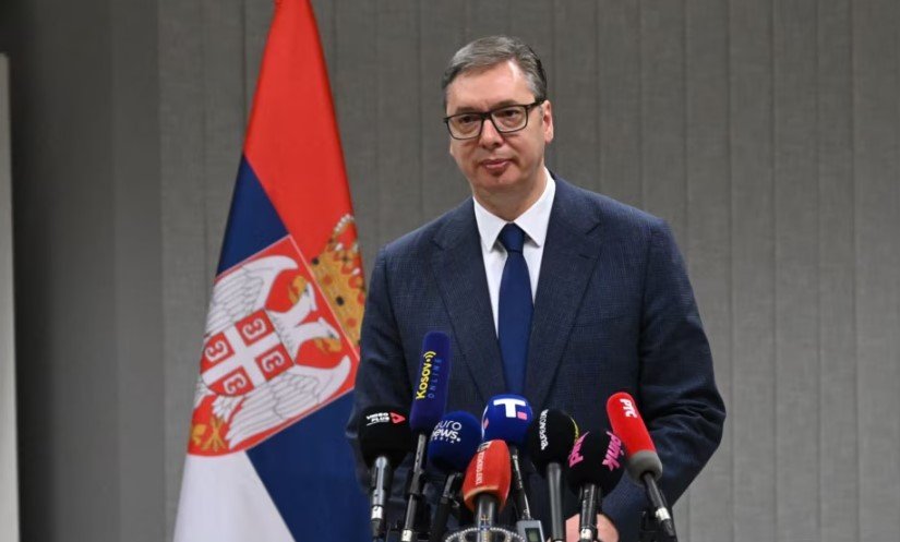 Serbian President Aleksandar Vucic at press conference with Serbian flag and media microphones