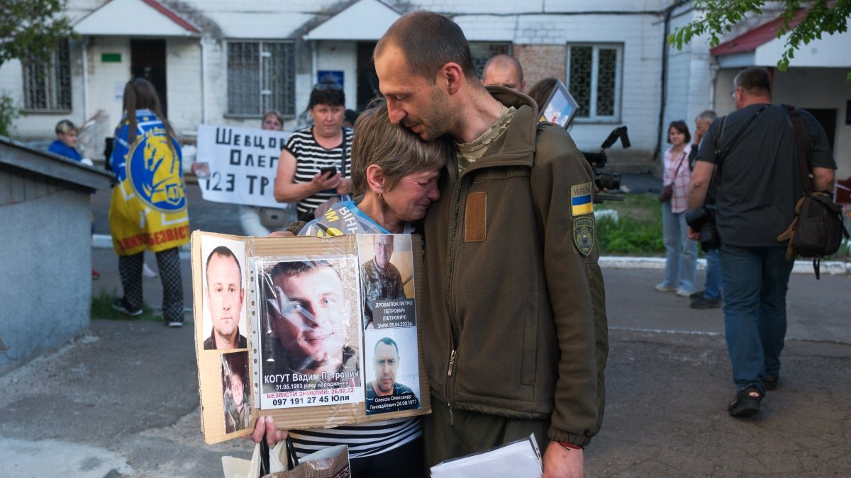 Family member holding photos of missing POWs, being comforted by soldier