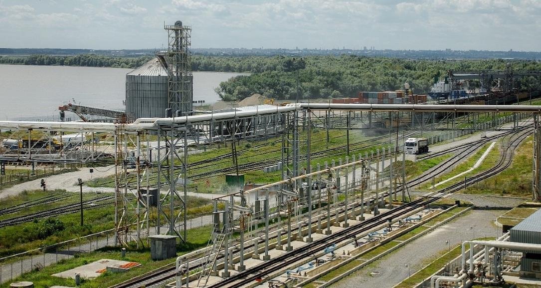Промышленная зона порта с железнодорожными путями, зерновым силосом, конвейерными системами и берегом Дуная на заднем плане