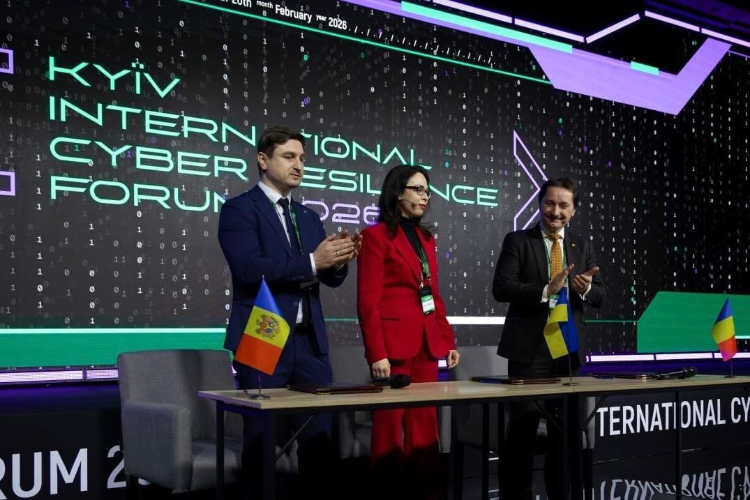 Three officials standing and applauding at the Kyiv International Cyber Resilience Forum after signing the agreement.