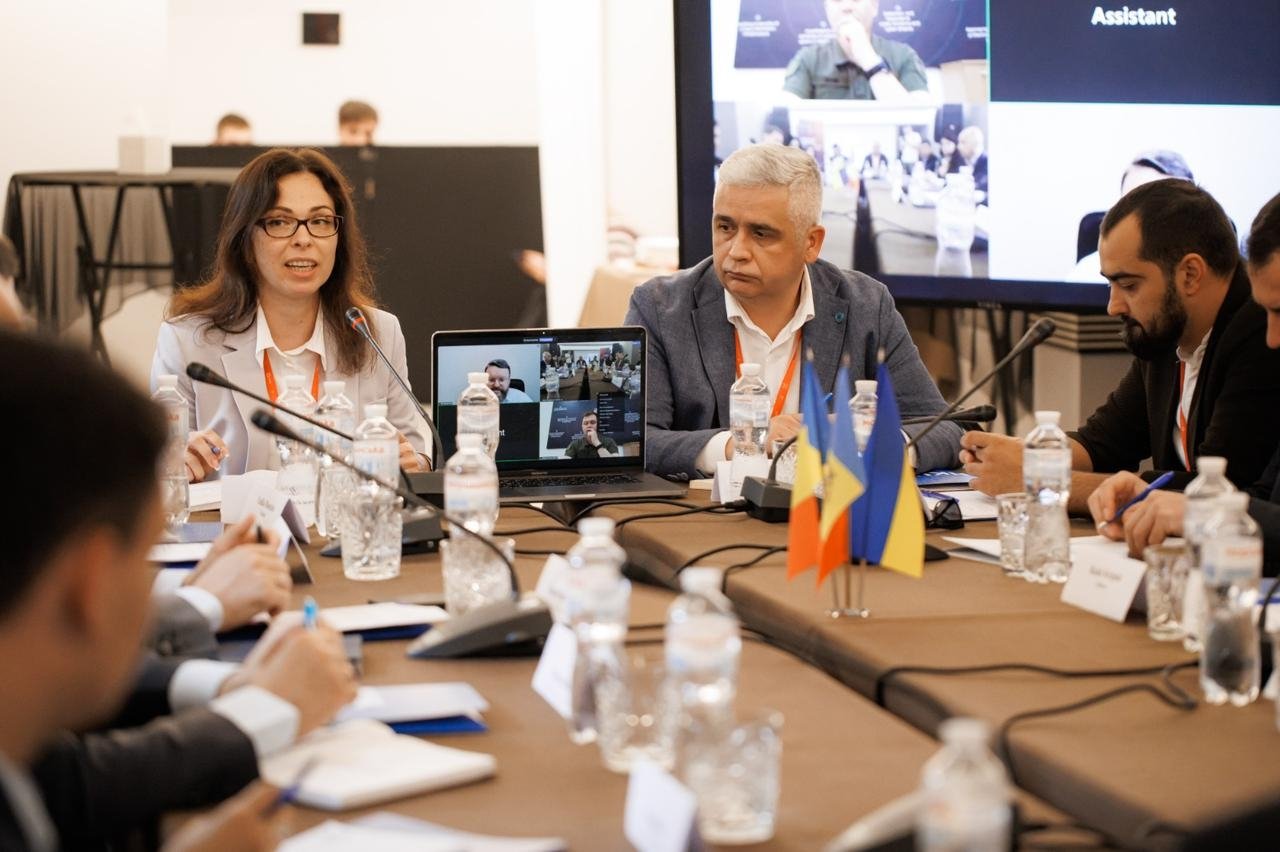 Working meeting of cyber alliance officials around a conference table with video conferencing, Ukrainian and Moldovan flags visible.