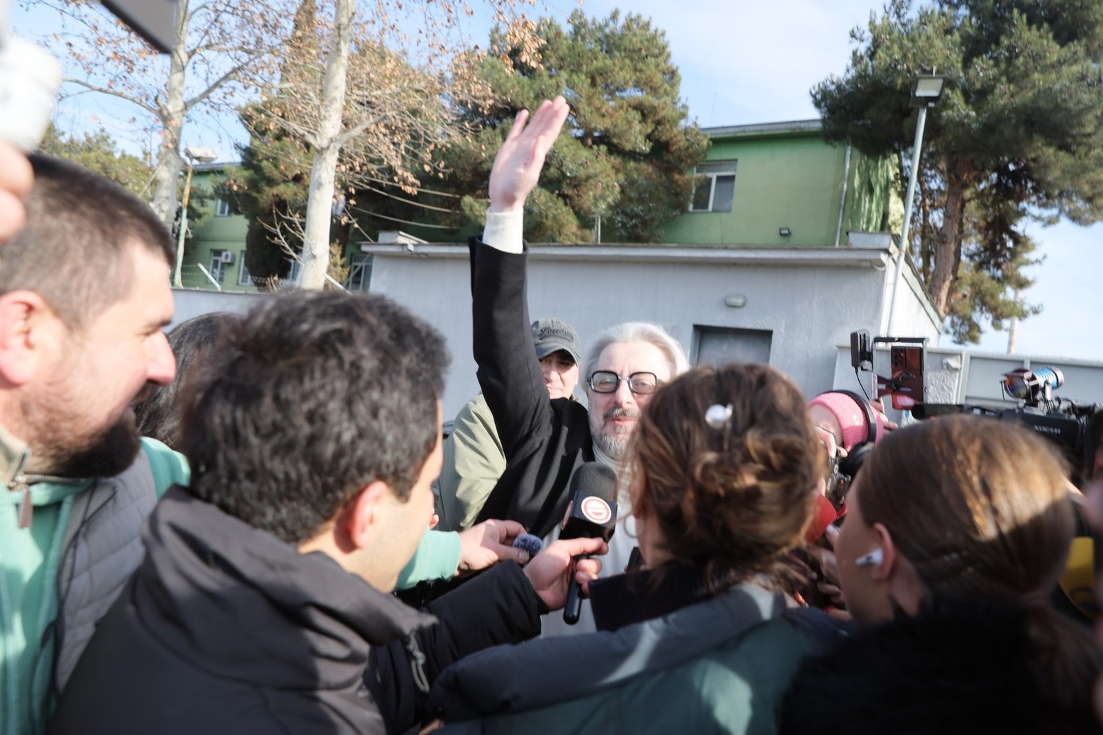 Мужчина поднимает руку в окружении журналистов и операторов