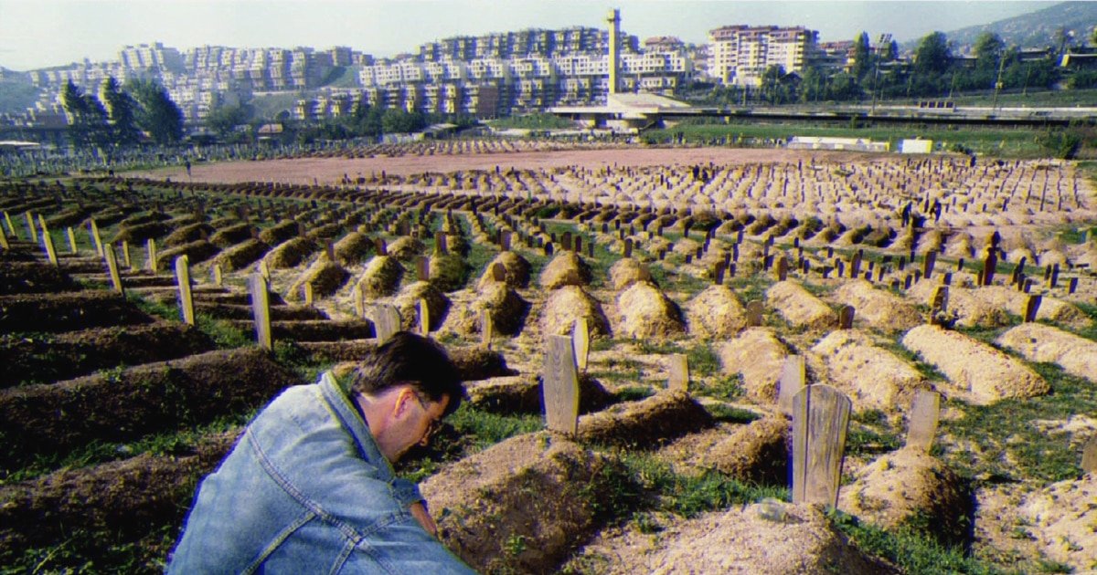 War cemetery in Sarajevo showing rows of fresh graves from the siege, with a mourner in the foreground