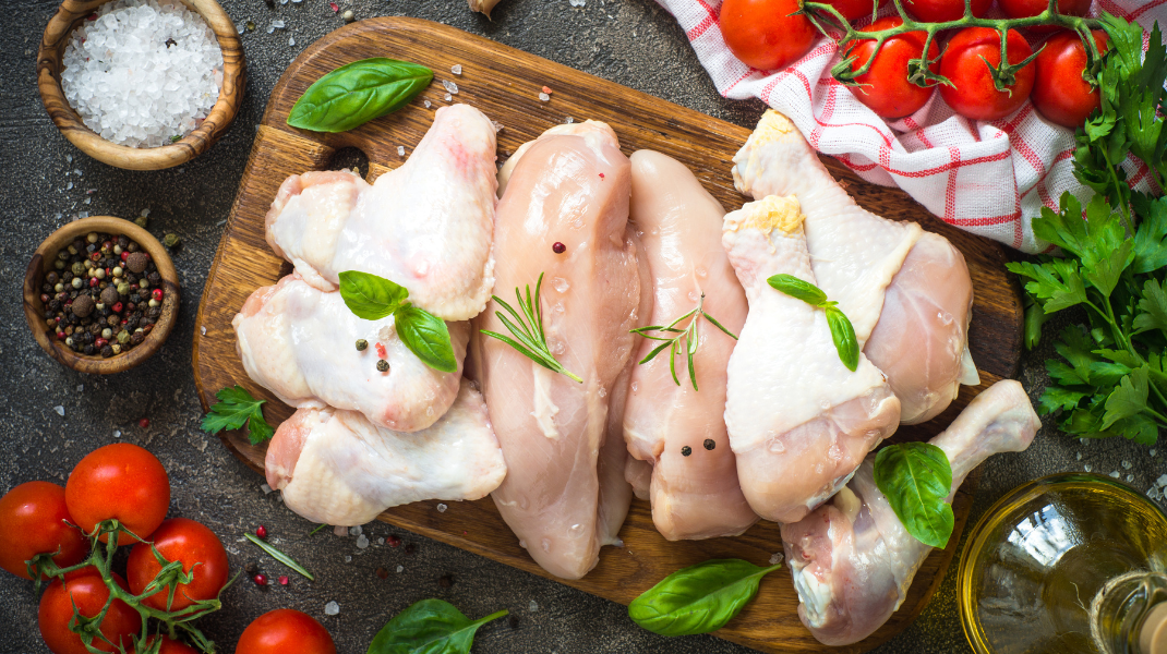 Raw chicken pieces on wooden cutting board with tomatoes, herbs and spices - food styling