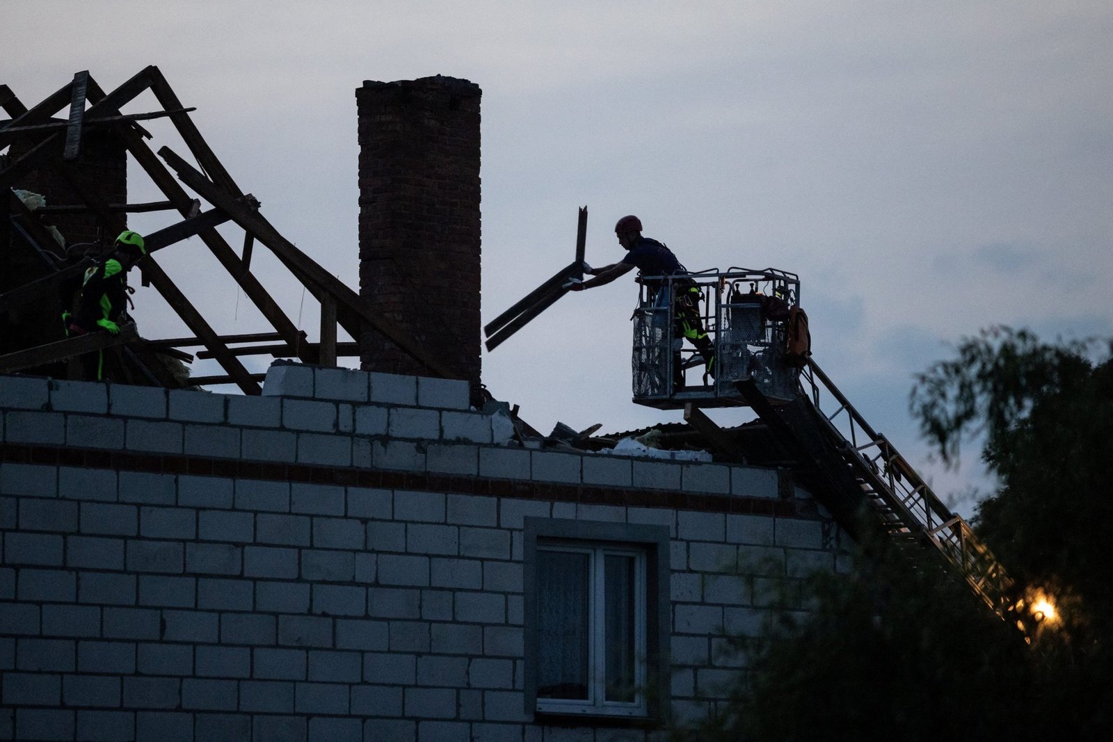 Workers repairing destroyed residential building roof at dusk - shows war damage and reconstruction efforts