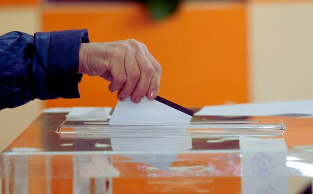 Hand putting ballot into voting box - illustrates voting theme