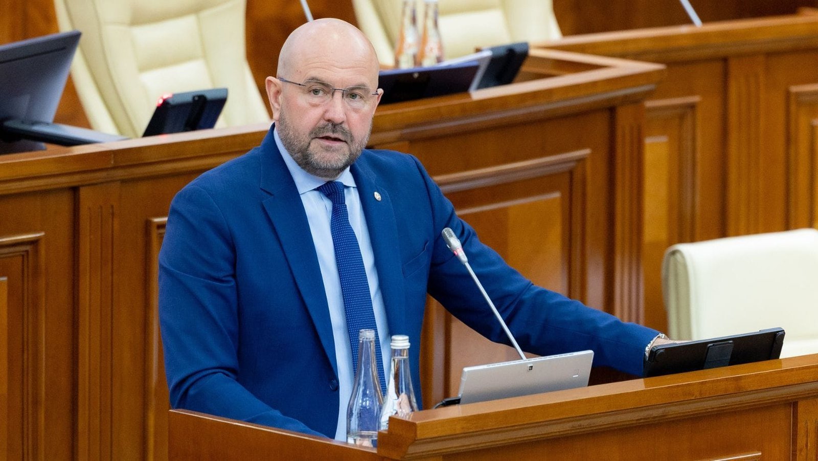 Министр Адриан Боля выступает с трибуны парламента в синем костюме