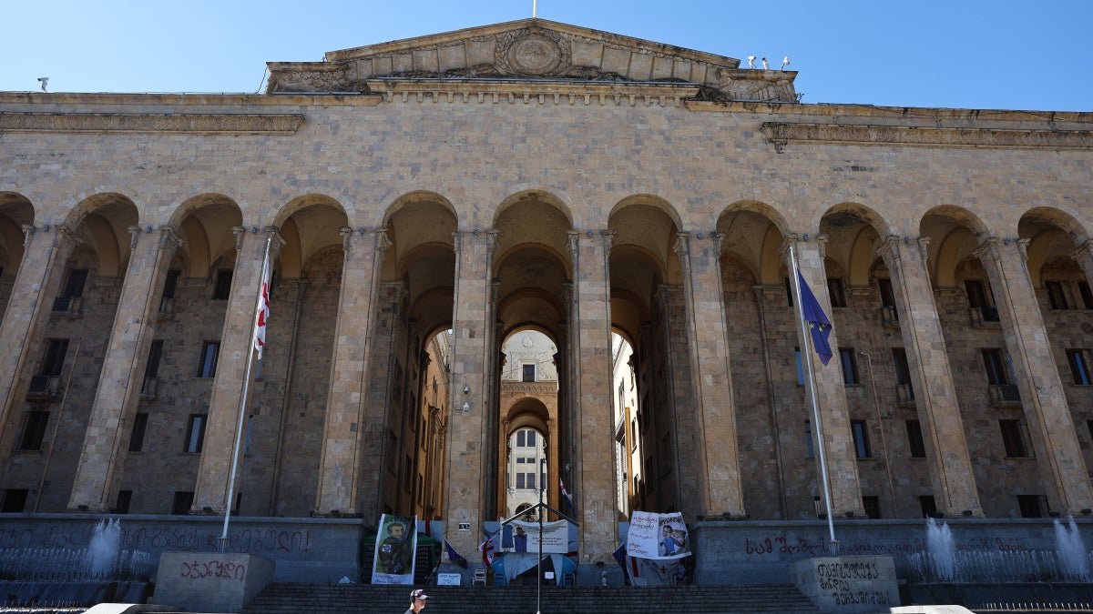 Здание парламента Грузии с флагами ЕС и Грузии, видны протестные баннеры