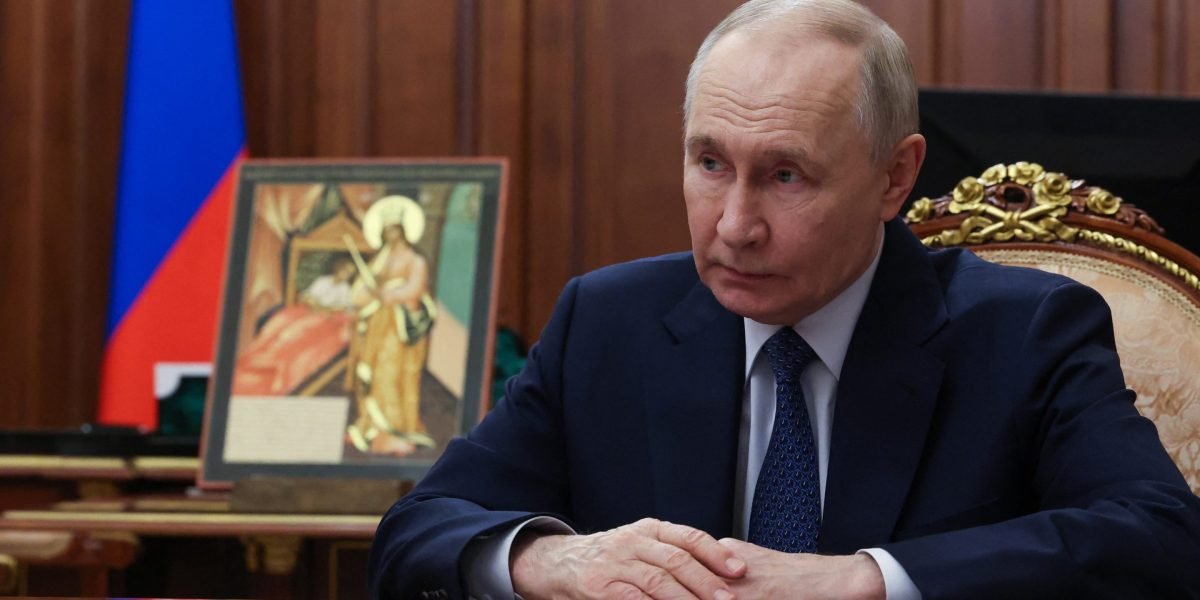 Владимир Путин за рабочим столом на фоне российского флага и иконы