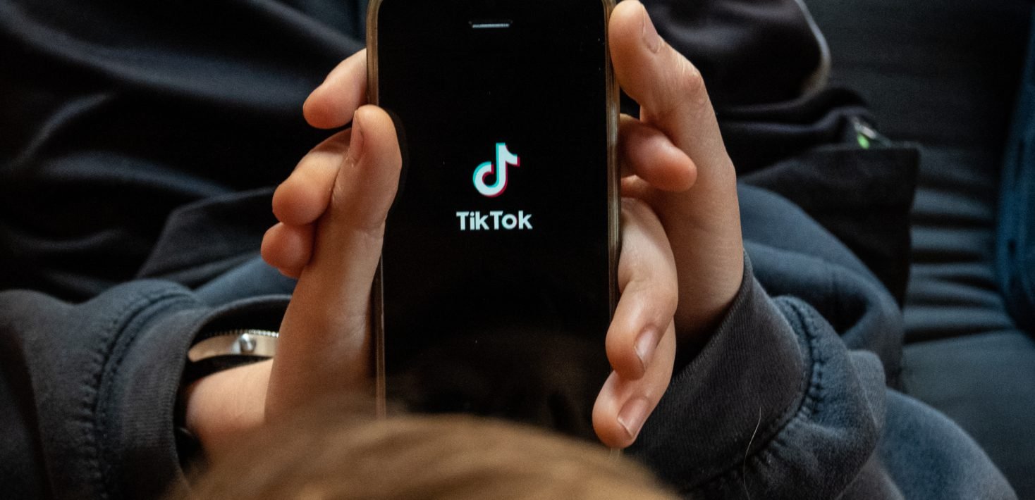 Young person holding phone showing TikTok logo — illustrates the addiction concern for minors