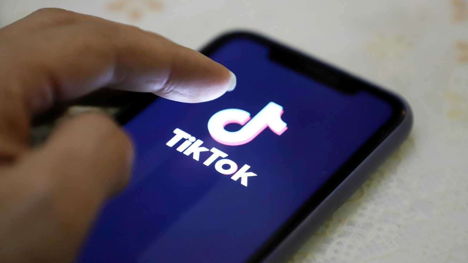 Finger tapping TikTok app on smartphone screen — shows the addictive interface interaction