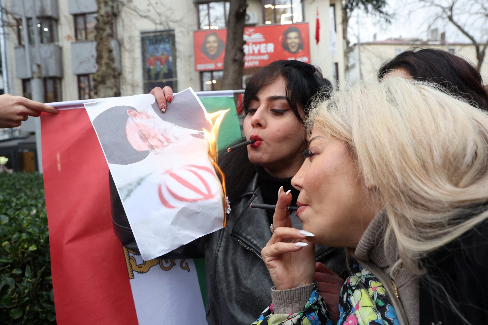Women protesters in Turkey burning portrait against Iranian flag backdrop, related to Iran tensions