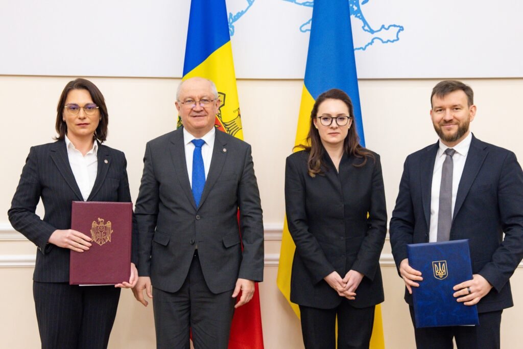 Четверо представителей Молдовы и Украины позируют с подписанными документами соглашения на фоне государственных флагов