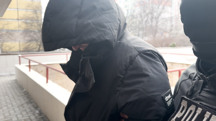 Nicolae Shepeli in black hood being escorted by police officer during arrest. Key suspect visual.