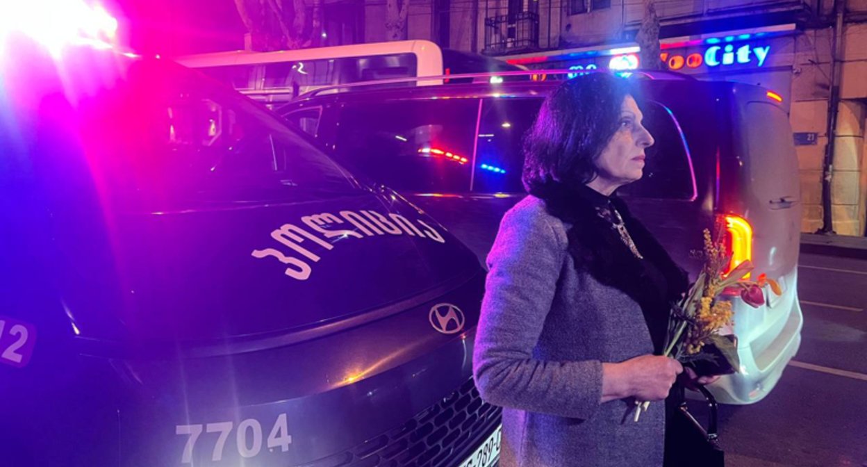 Женщина с цветами у полицейского фургона ночью в Тбилиси