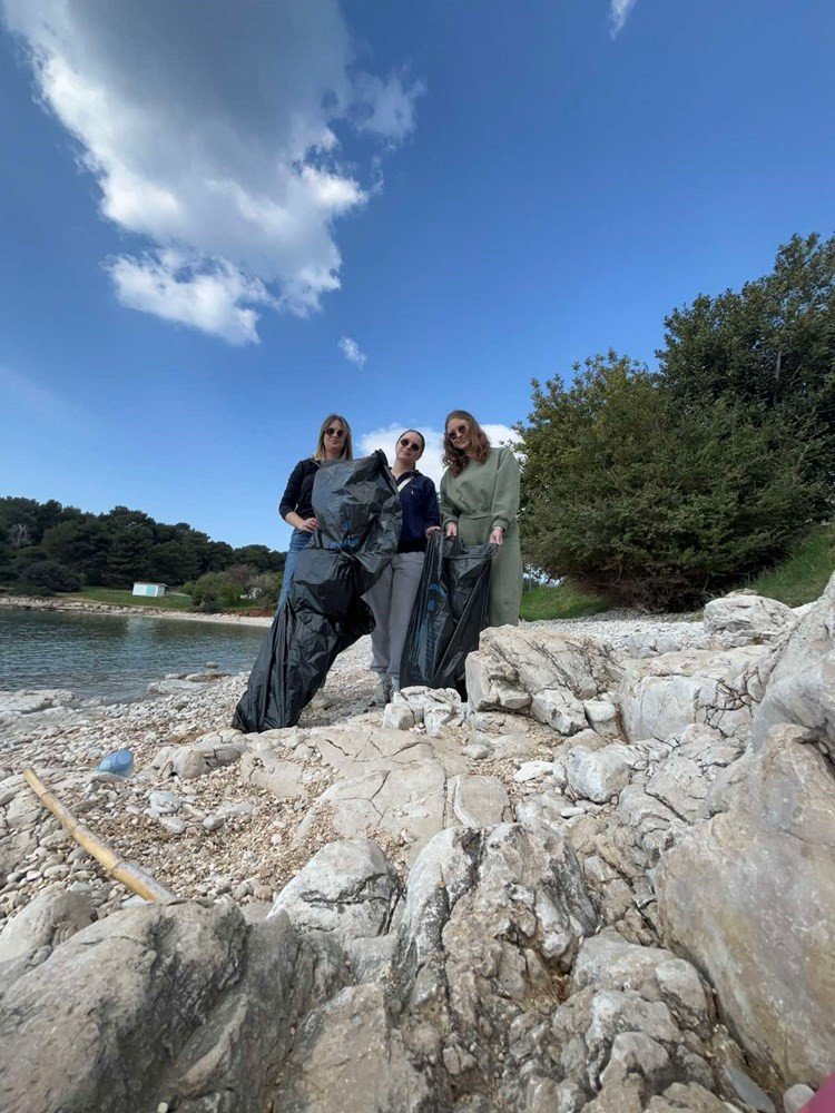 Три студентки с мешками для мусора на каменистом берегу Истрии — волонтёрская уборка побережья в рамках проекта Blue Connect