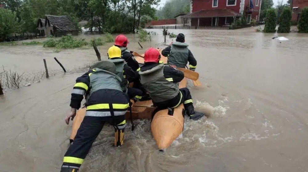 Спасательная операция при наводнении: пожарные в защитном снаряжении толкают надувную лодку по затопленной улице деревни. Фото: Danas