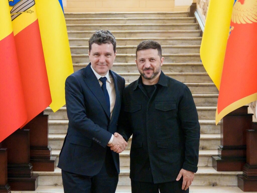 Президент Украины Владимир Зеленский и президент Румынии Никушор Дан обмениваются рукопожатием на парадной лестнице в Бухаресте на фоне флагов Румынии и Украины