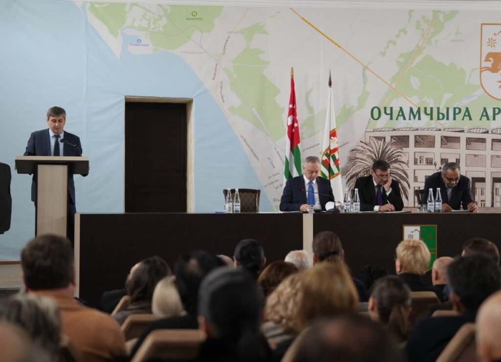 Заседание районного собрания Очамчырского района Абхазии — чиновник выступает с докладом об исполнении бюджета на фоне карты Очамчиры и абхазского флага