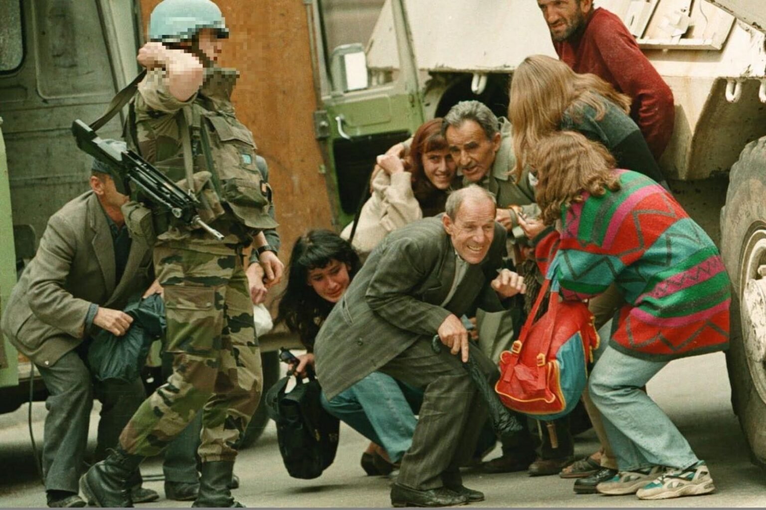 Мирные жители Сараево пригибаются под снайперским огнём под прикрытием миротворца ООН во время осады города в 1990-х годах