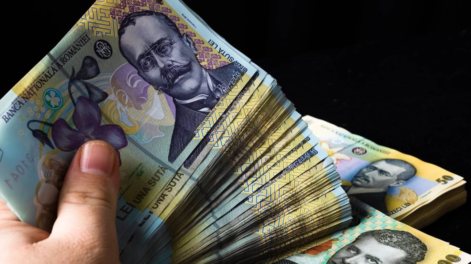 Пачка румынских банкнот номиналом 100 леев в руке на тёмном фоне
