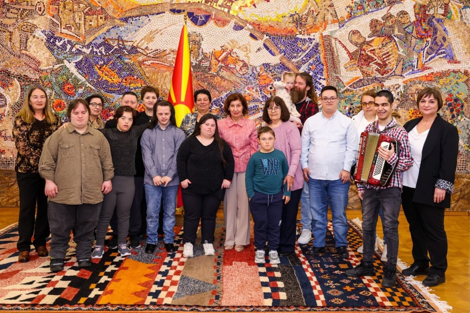 Групповое фото президента Силяновской-Давковой с представителями сообщества людей с синдромом Дауна на фоне мозаичного панно в президентском дворце
