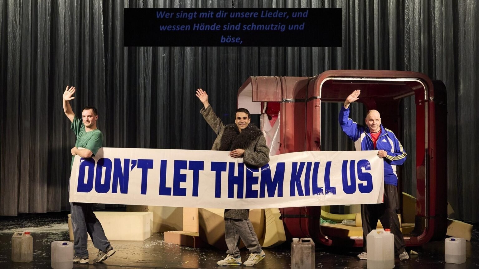 Актёры Даниэль Клауснер, Лука Димич и Клаус Мюллер-Бек держат плакат «DON'T LET THEM KILL US» в спектакле «Радио Сараево» на сцене Ландестеатра Линца