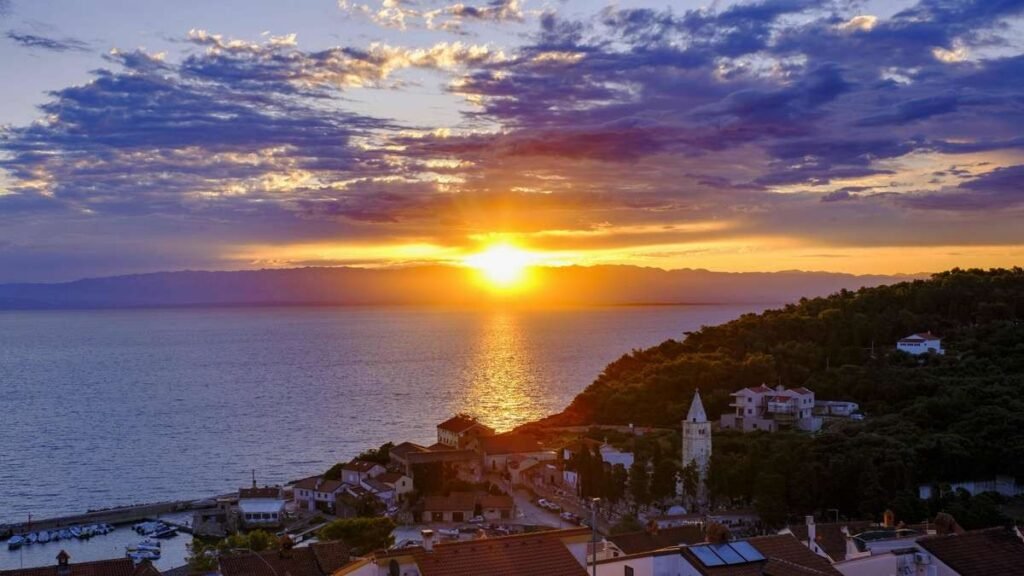 Закат над курортным посёлком на Адриатическом побережье Хорватии — черепичные крыши, церковная колокольня и небольшая гавань