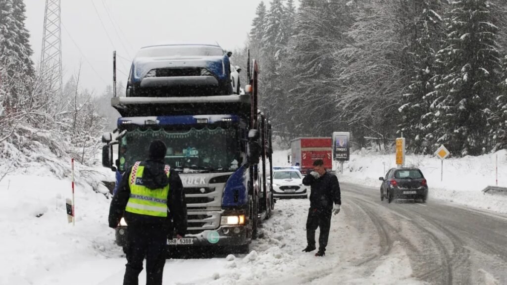 Грузовик-автовоз на заснеженной горной дороге в Хорватии, рядом работают полиция и дорожные службы