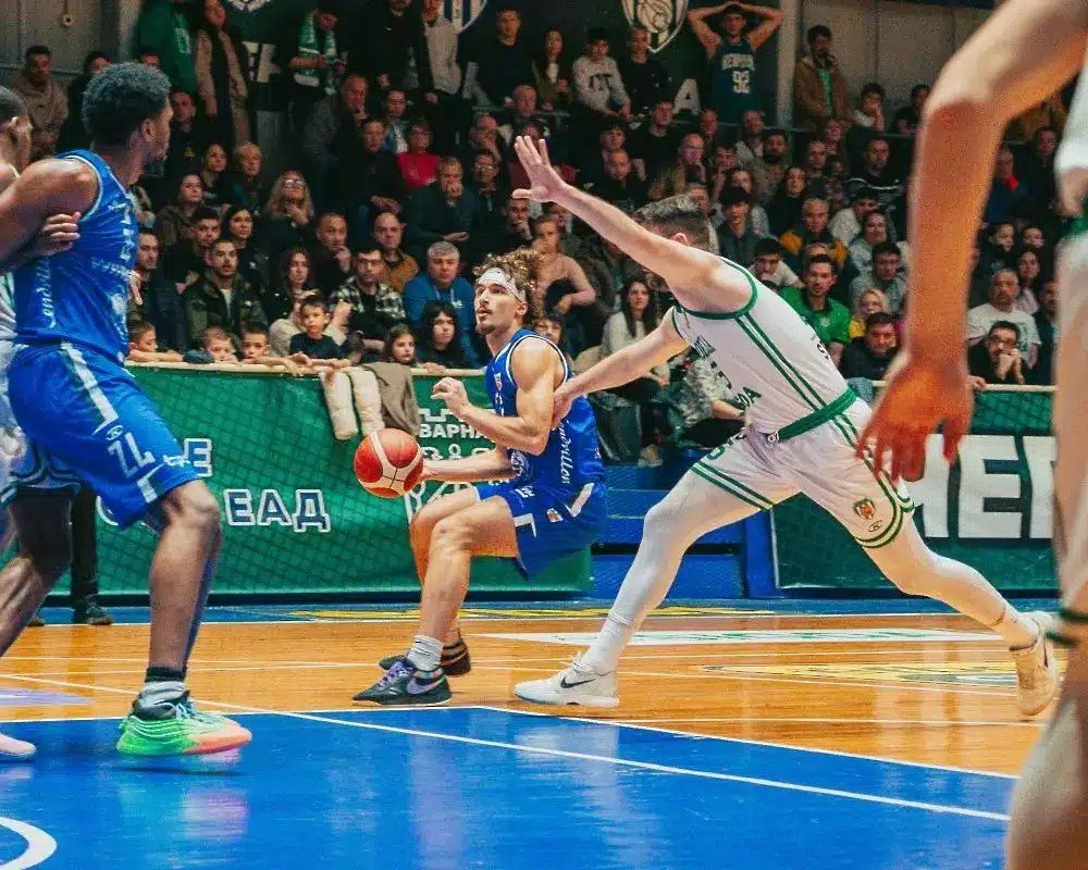 Спартак Плевен: шестая победа подряд в чемпионате Болгарии Баскетболист «Спартак Плевен» в синей форме ведёт мяч мимо защитника «Черно море Тича» в матче 28-го тура НБЛ во Варне