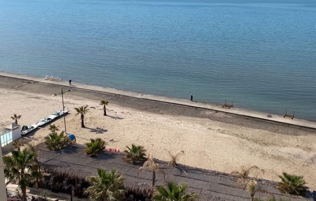 Вид сверху на пляж с пальмами и набережной на побережье Албании