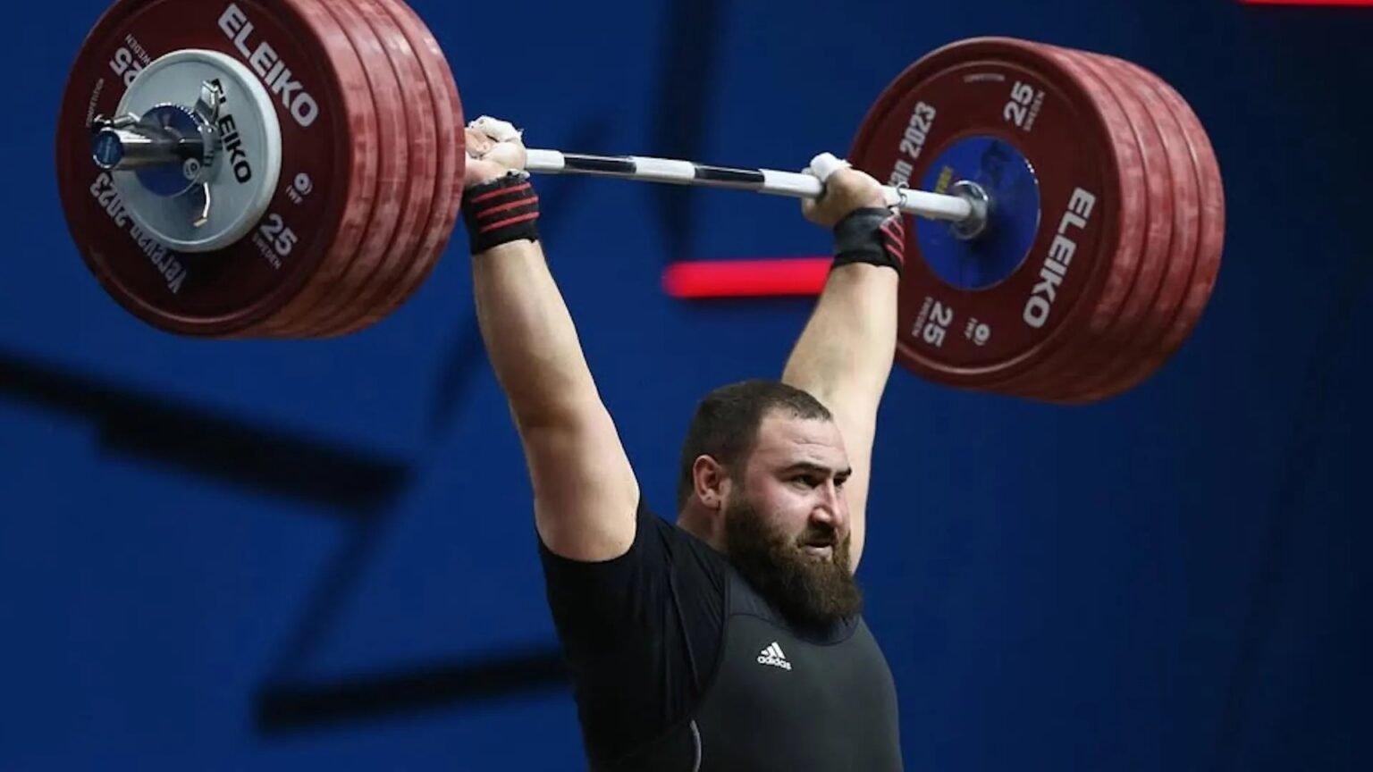 Батуми примет чемпионат Европы по тяжёлой атлетике Тяжелоатлет выполняет рывок штанги на соревнованиях — оборудование ELEIKO на фоне синего зала