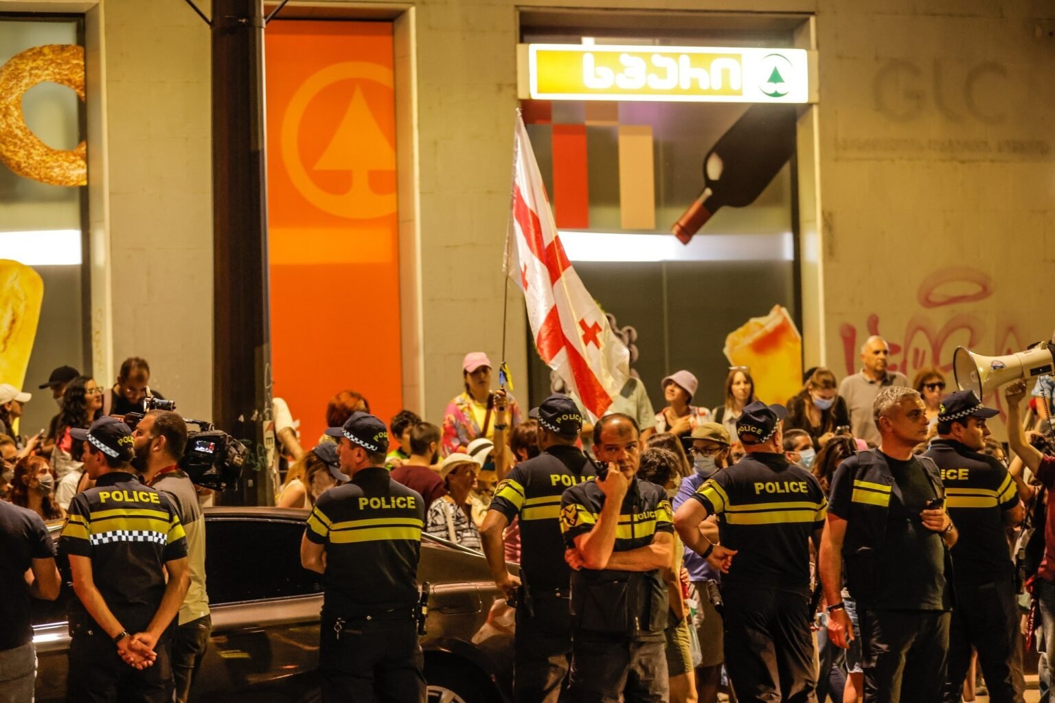Полицейские в ряд на ночном протесте с грузинским флагом на заднем плане. Фото: NewsGeorgia.ge