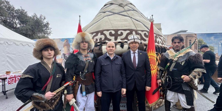 Официальные лица и участники в традиционных кыргызских костюмах позируют на фоне украшенной юрты с кыргызскими флагами на выставке у Девичьей башни в Баку