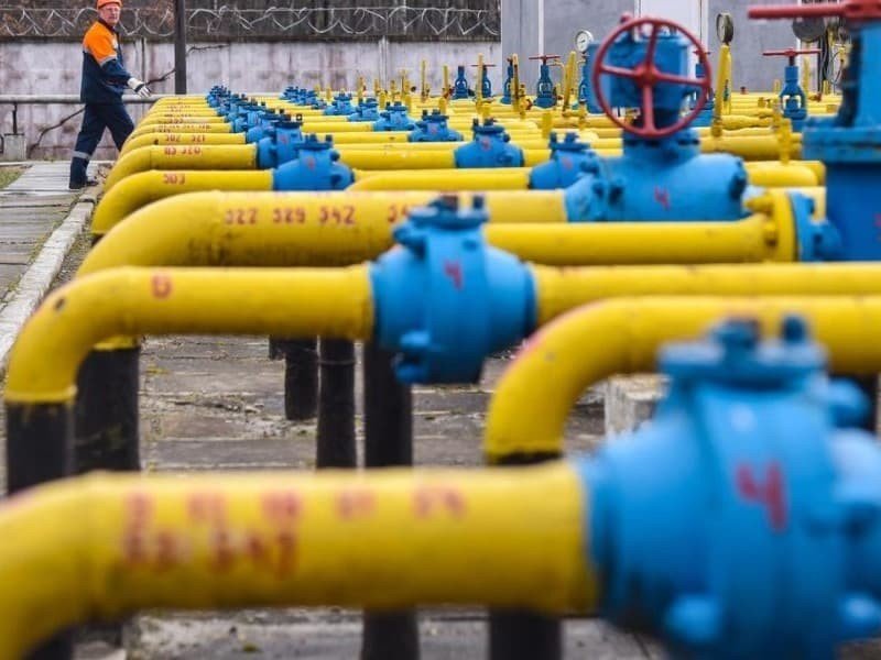 Желтые газовые трубы с синими вентилями на газораспределительной станции, рабочий в оранжевом жилете. Фото: D32r1sh890xpii.cloudfront.net