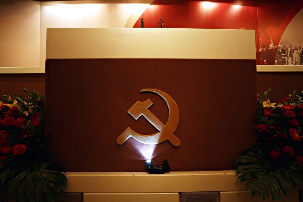 Греция на перепутье: КПГ требует закрыть базы НАТО на фоне иранских ударов Трибуна КПГ с эмблемой серпа и молота, украшенная красными цветами. Фото: 902.gr